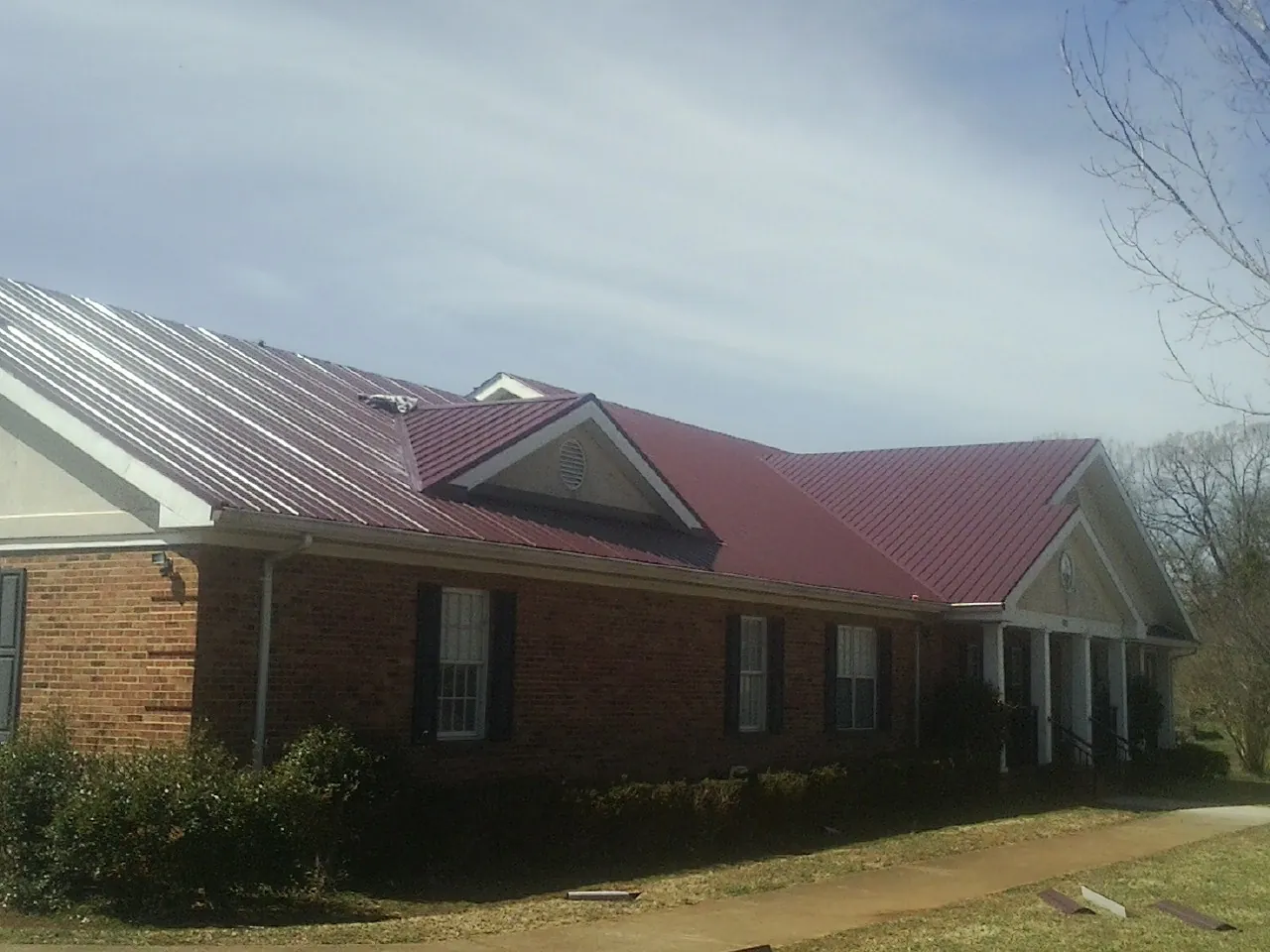 Red metal roof with gabled entries on a long brick building, from a Hail Damage Roof Repair job in Berea