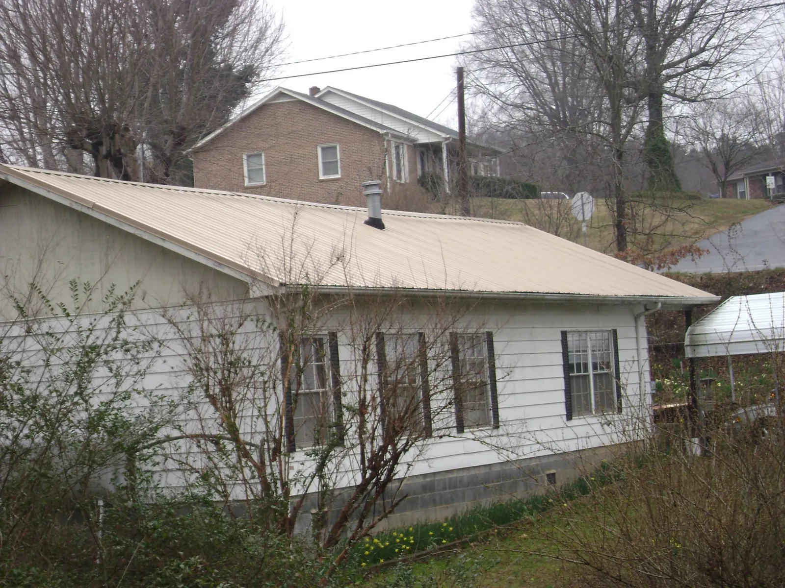 Tan metal roof on a white sided house set into a hillside — Commercial Roofing by Roofing Brothers in Berea